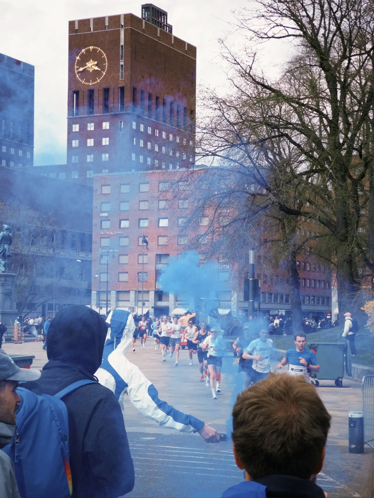 Runners passing through blue smoke in front of Oslo City Hall