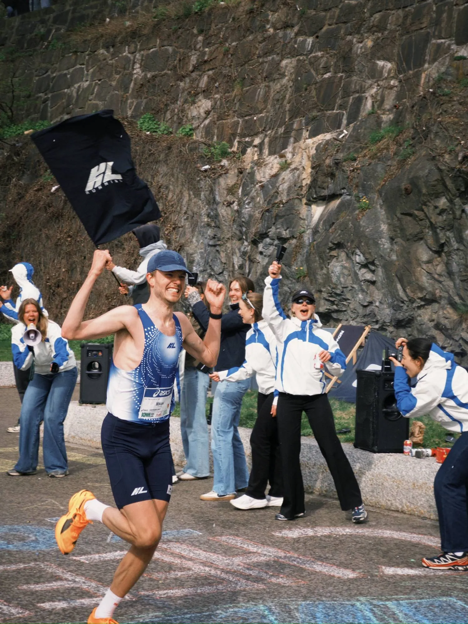 A KL runner sprinting past the team cheering with flag and megaphone